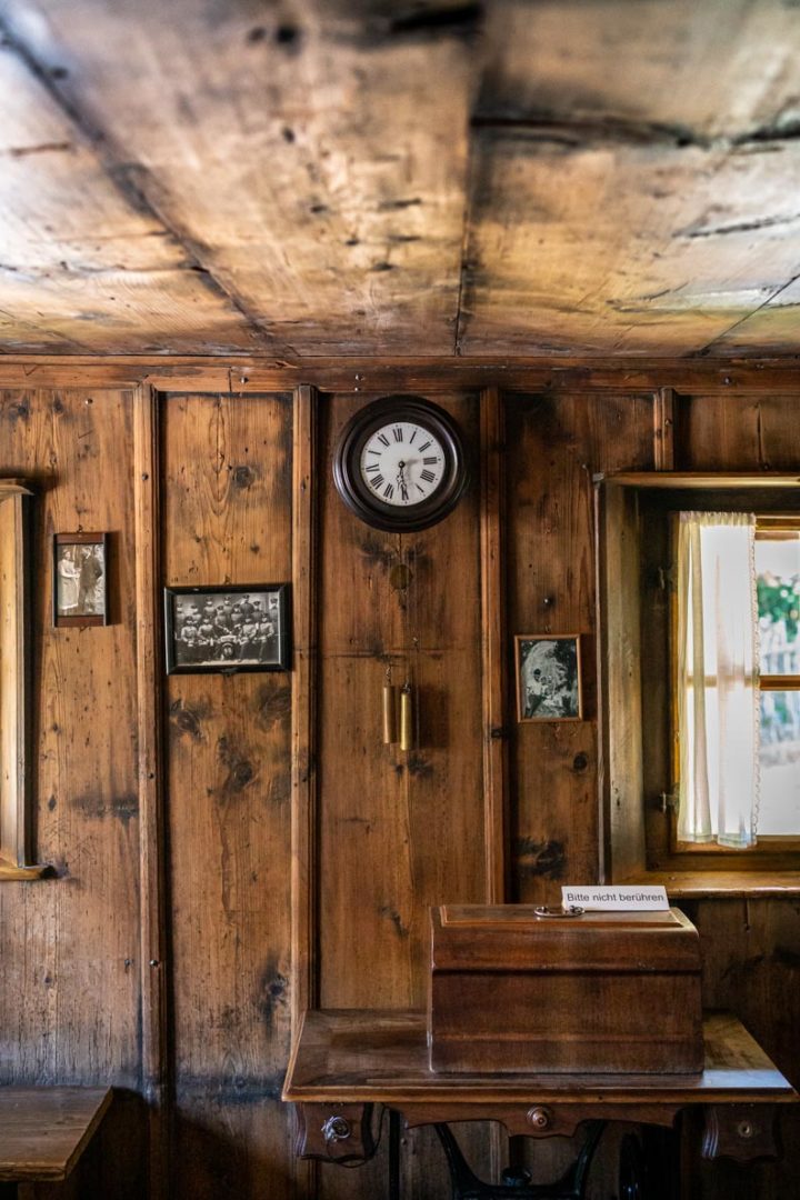 Eine alte Holzwand mit historischer Uhr und Bildern in einem traditionellen Bauernhaus
