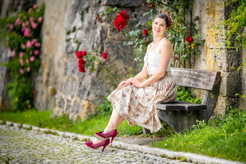 RetroCat wearing a rose skirt and white top by Lena Hoschek in front of a rose wall