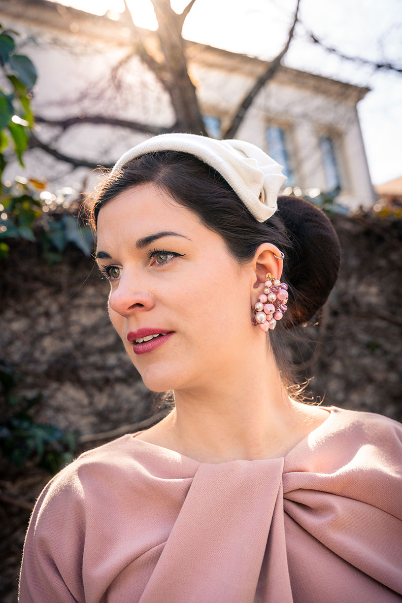 RetroCat wearing a light pink dress, half hat and vintage earrings