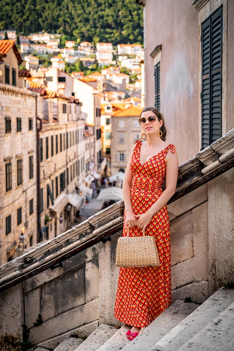 RetroCat mit buntem Maxikleid, großer Sonnenbrille und einer Korbtasche in Dubrovnik