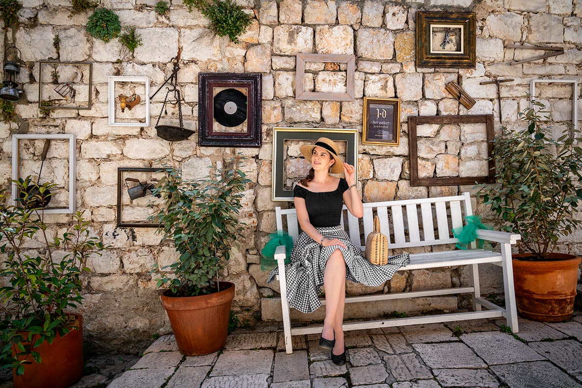 RetroCat wearing a vichy skirt and straw hat on a bench in Sibenik/Croatia