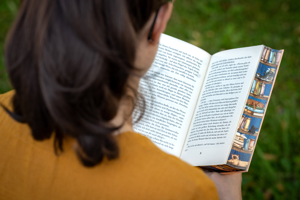 RetroCat liest ein Cozy Fantasy Buch von Heather Fawcett mit Farbschnitt