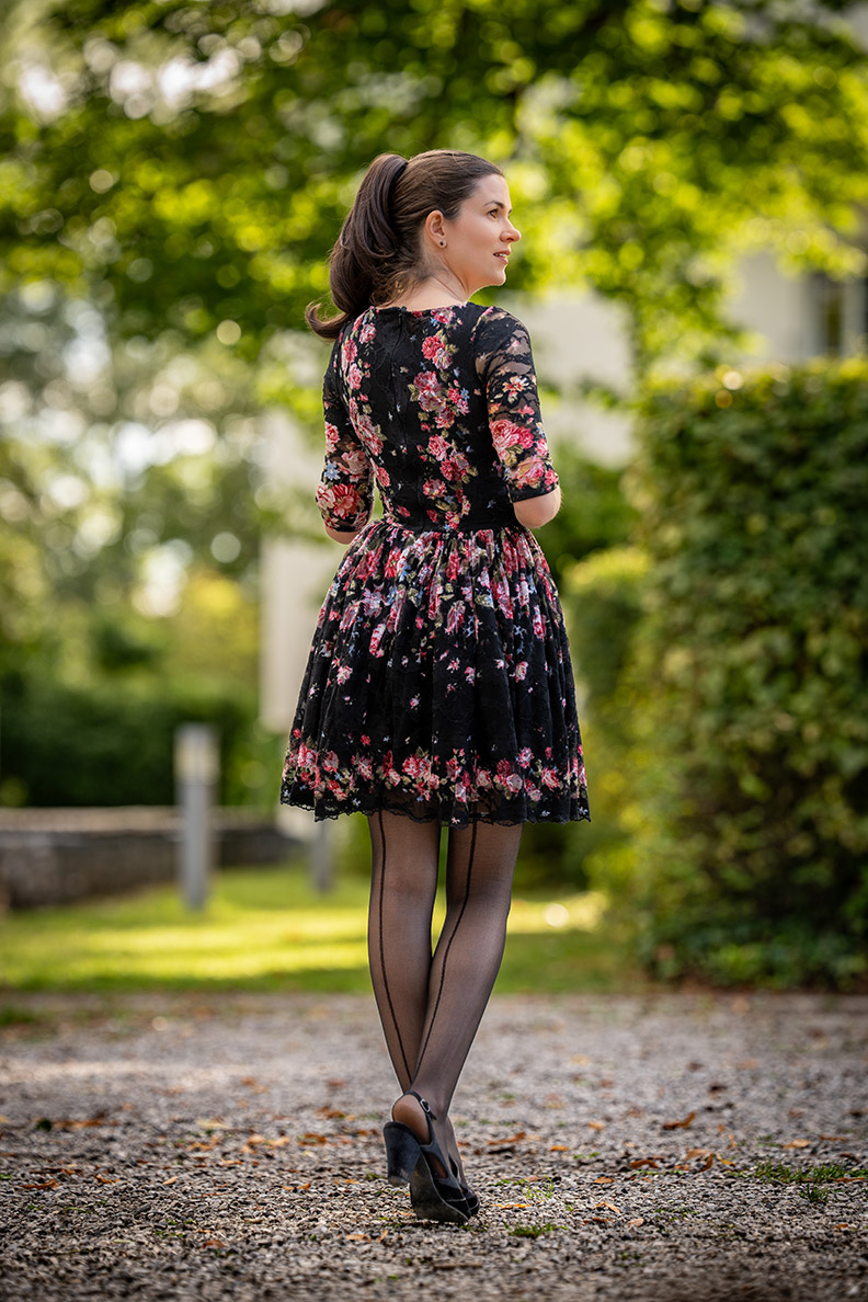 RetroCat wearing a black dress with rose pattern and seamed tights in late summer